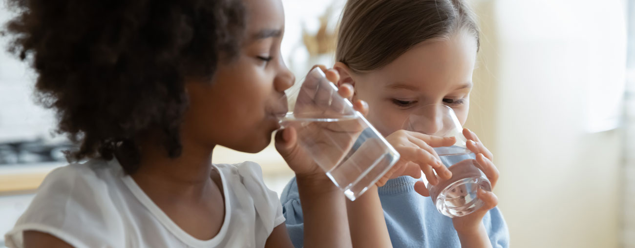 Två barn som dricker vatten ur varsitt glas.