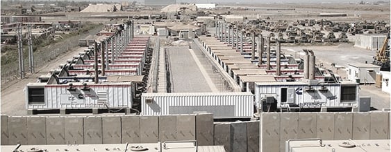 Exterior view of row of diesel generators behind a cement barricade 