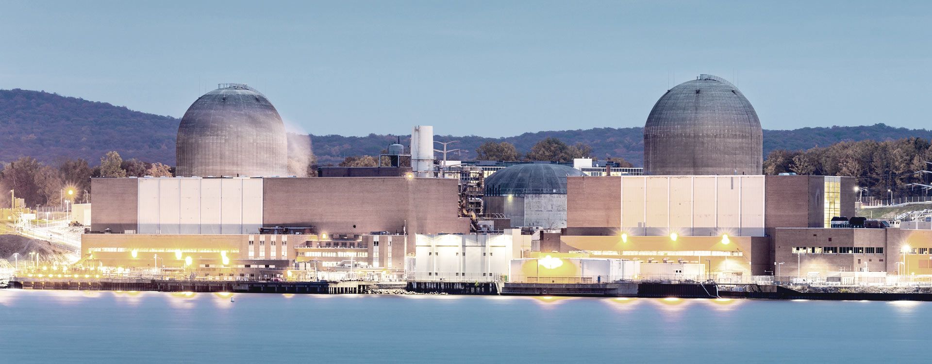 Upplyst kärnkraftverk sett från havet i skymning
